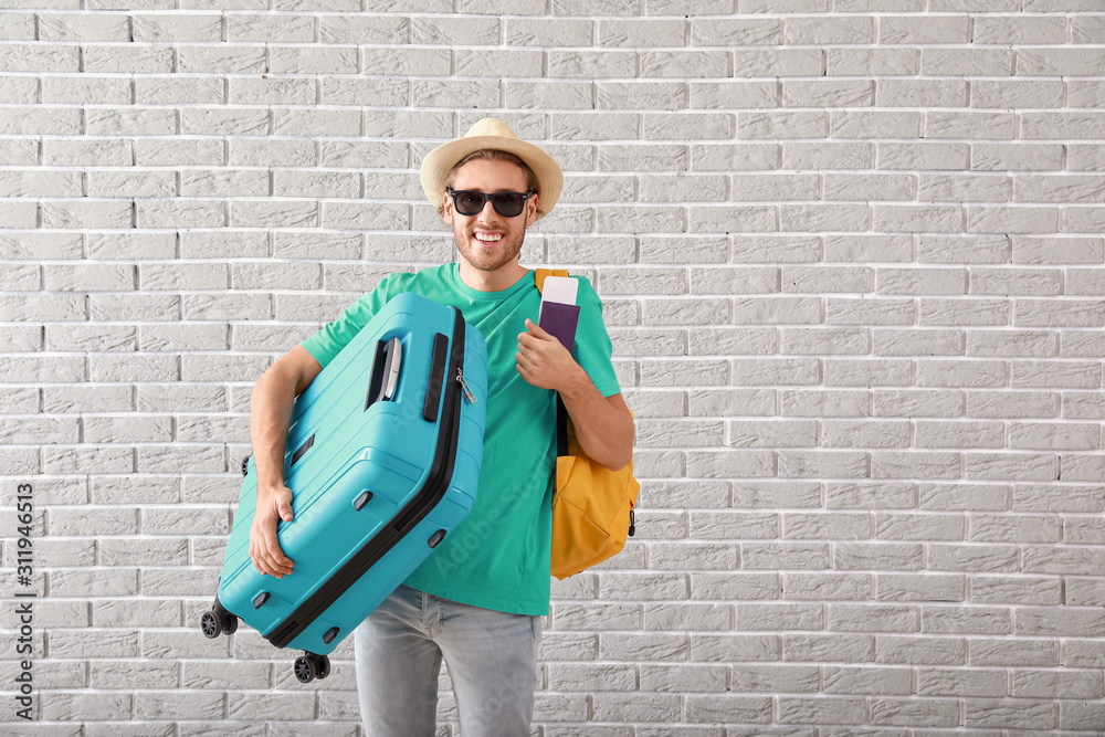 Young man with luggage near brick wall