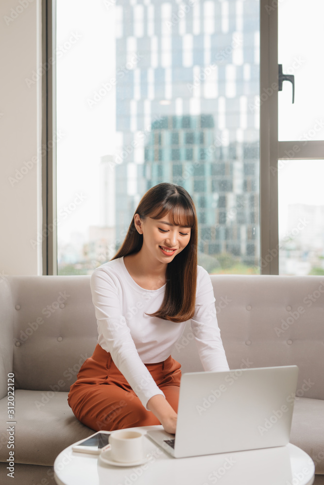 穿着休闲服的年轻女子坐在舒适的家里的沙发上。技术和通信公司