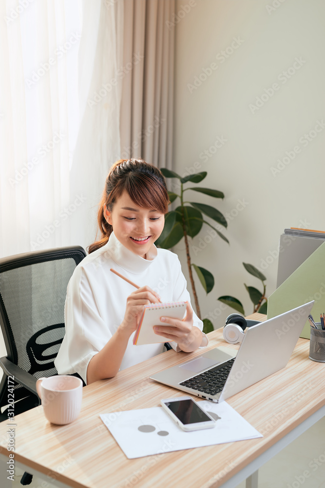 漂亮的年轻亚洲女人在家用笔记本电脑写笔记本