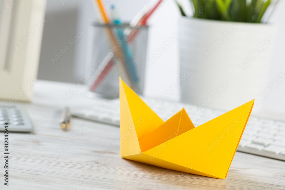 Businessman desk with yellow paper ship