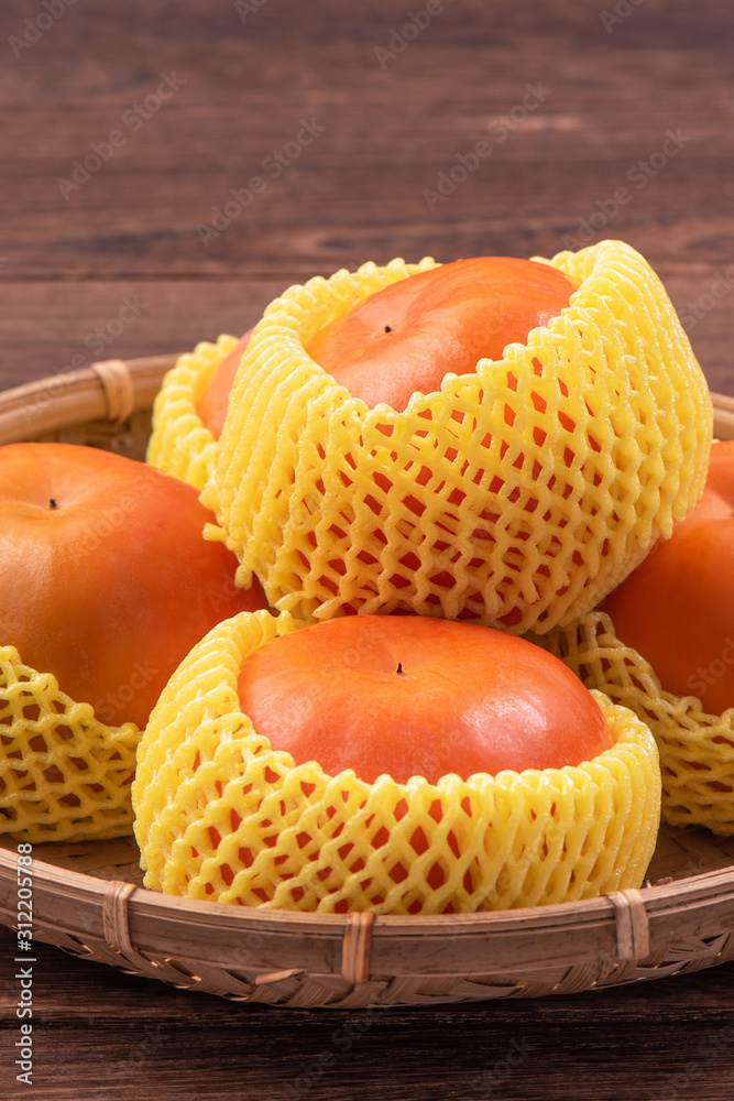 Fresh, beautiful orange color persimmon kaki on bamboo sieve over dark wooden table. Seasonal, tradi