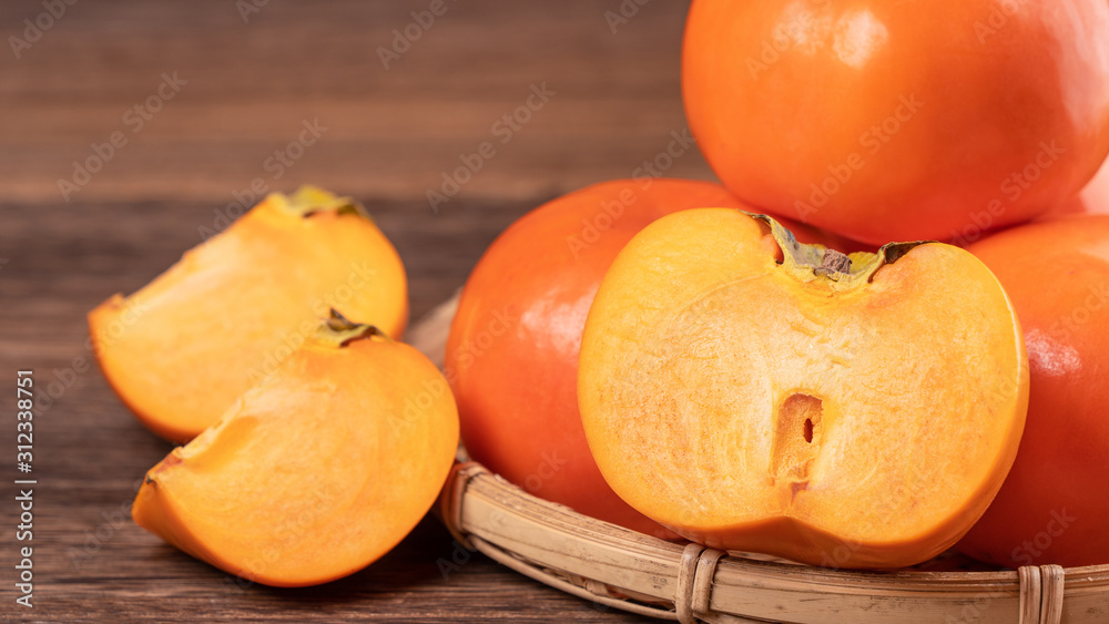 Fresh, beautiful orange color persimmon kaki on bamboo sieve over dark wooden table. Seasonal, tradi