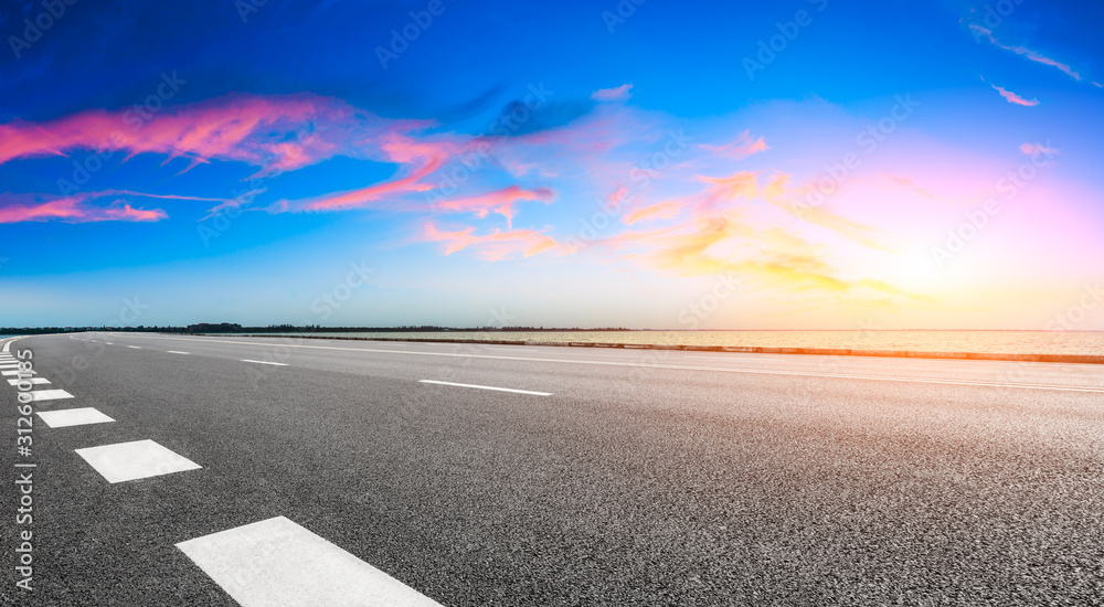 空旷的柏油路和湖面，日落时有梦幻般的云朵。