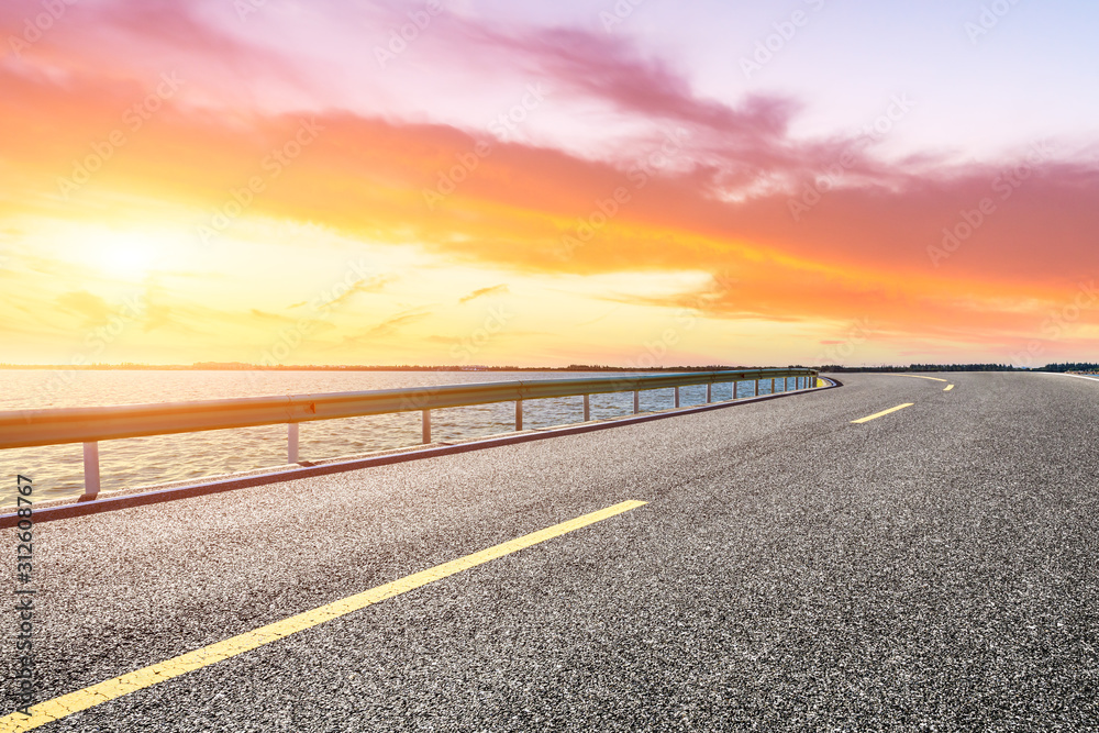 Empty asphalt road and lake with dreamy clouds at sunset.