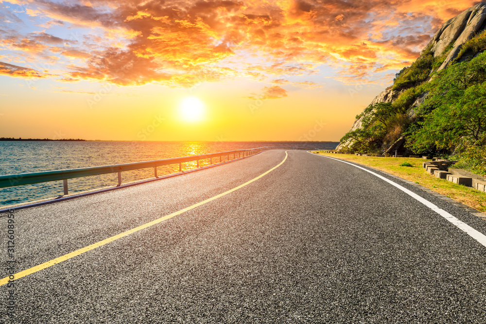 Empty asphalt highway and lake with mountains at beautiful sunset.