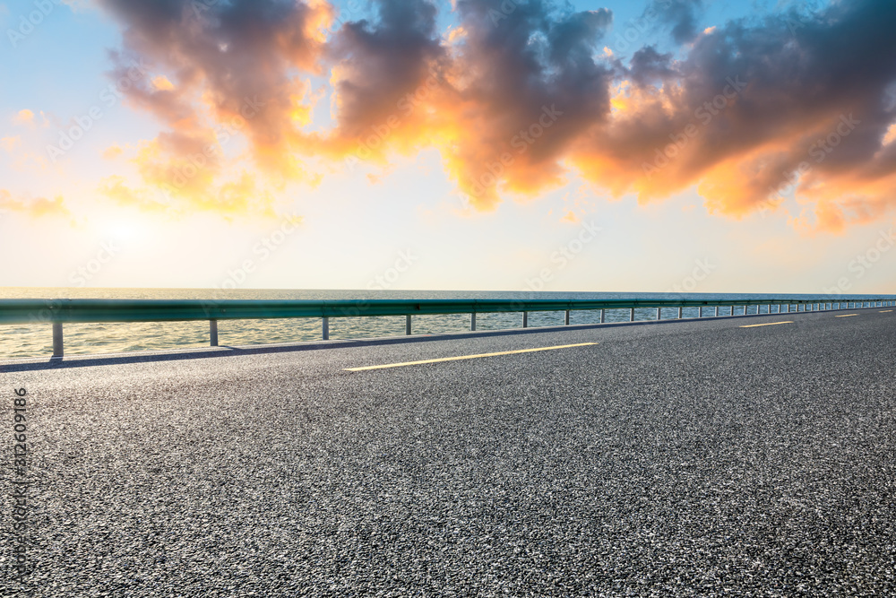 Empty asphalt road and lake with dreamy clouds at sunset.