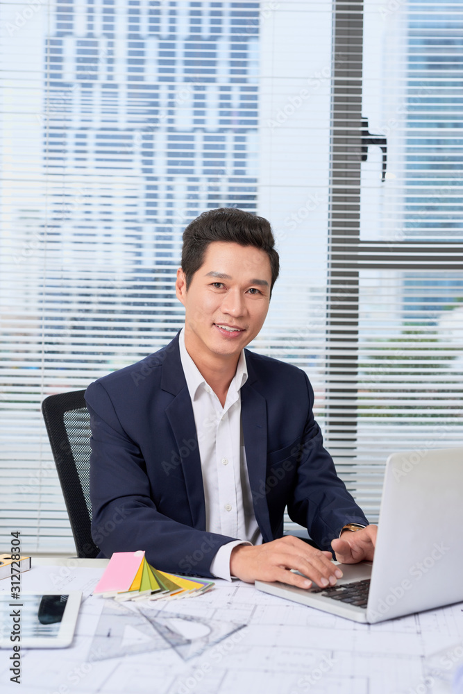 portrait of a nice smiling man, working at home on some project, he is sitting at a white table look