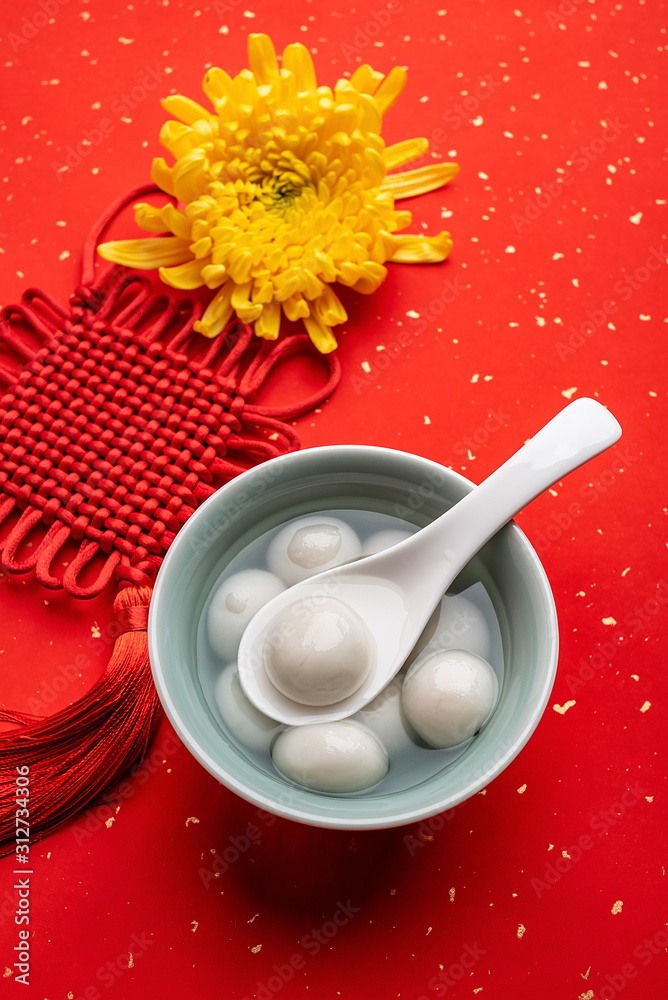 洒红纸背景上的中国元宵美食饺子和如意结