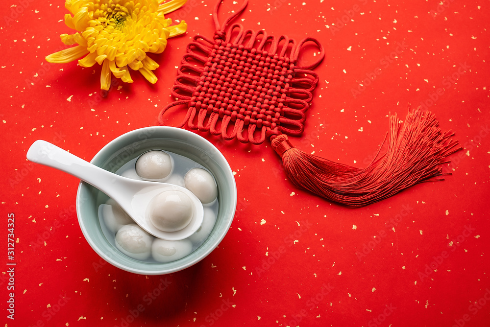 洒红纸背景上的中国元宵美食饺子和如意结