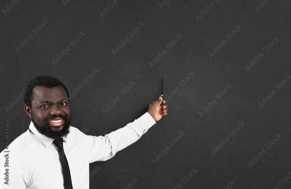 African-American teacher pointing at something on blackboard in classroom