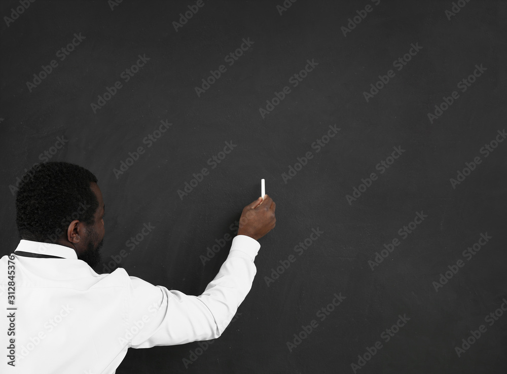 African-American teacher writing on blackboard in classroom