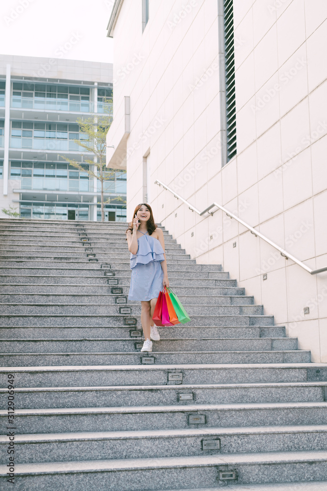 漂亮女孩下楼梯时拿着购物袋打电话。