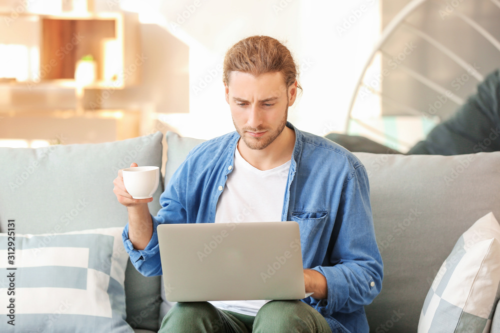 Handsome man with laptop drinking coffee at home