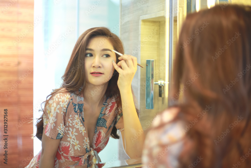 Beautiful Asian woman using eyebrow pencil make up in front mirror.