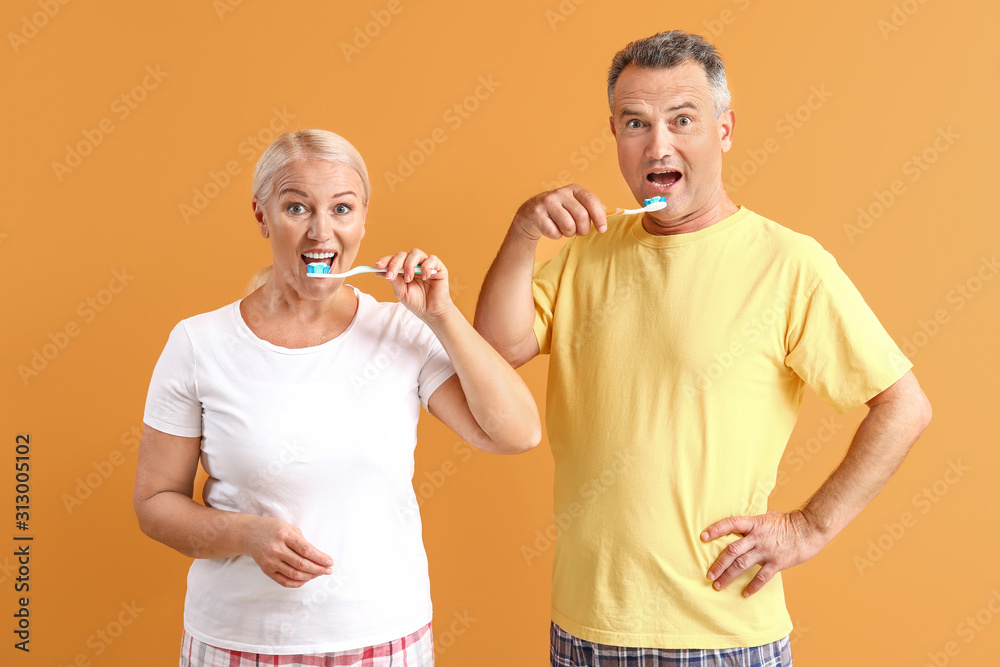 Mature couple brushing teeth on color background