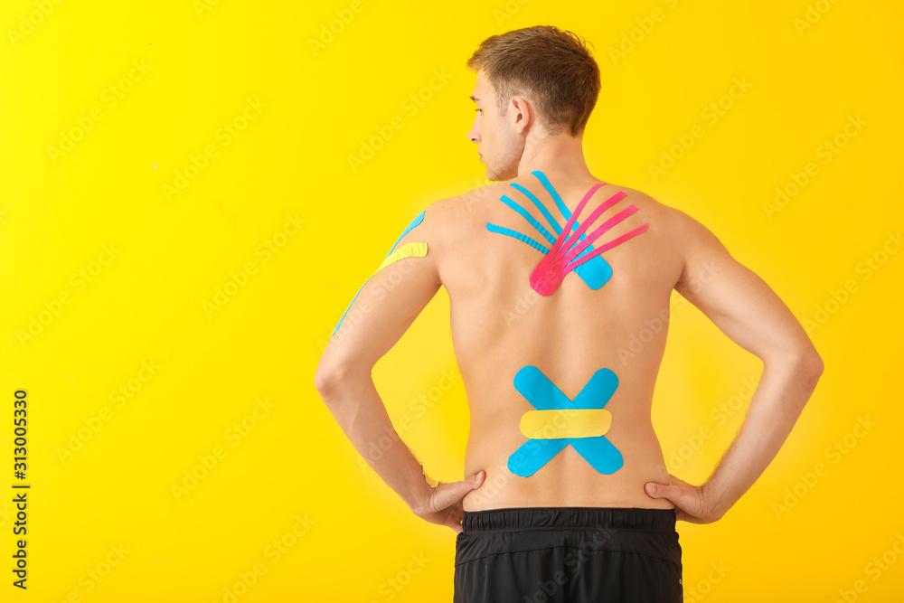 Sporty man with physio tape applied on back against color background