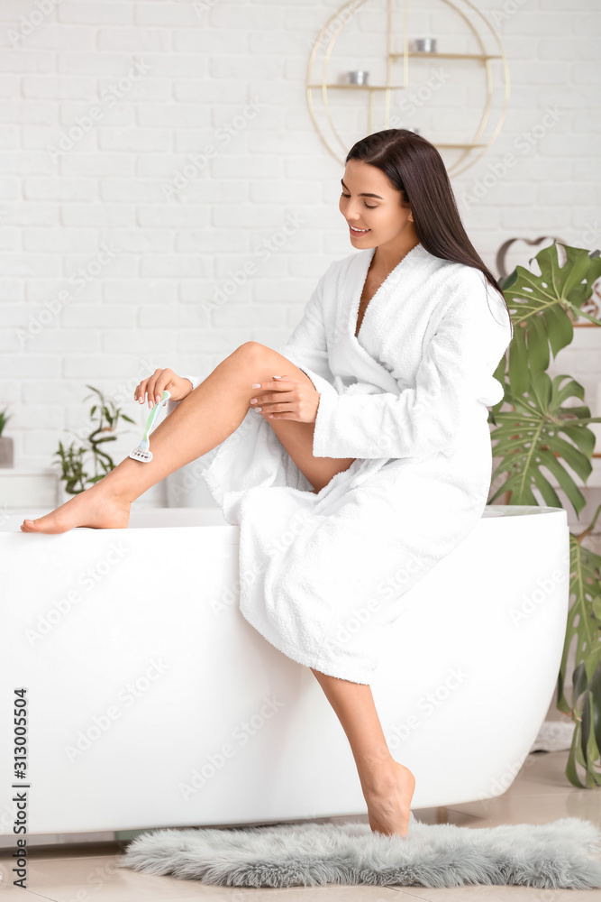 Beautiful young woman shaving legs in bathroom