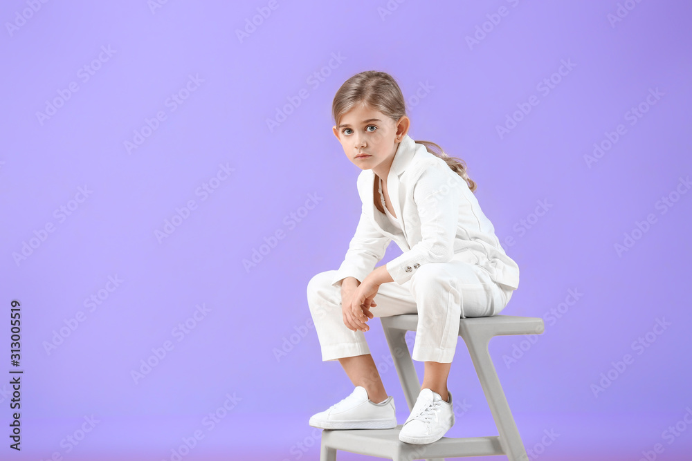 Cute little girl in autumn clothes sitting against color background