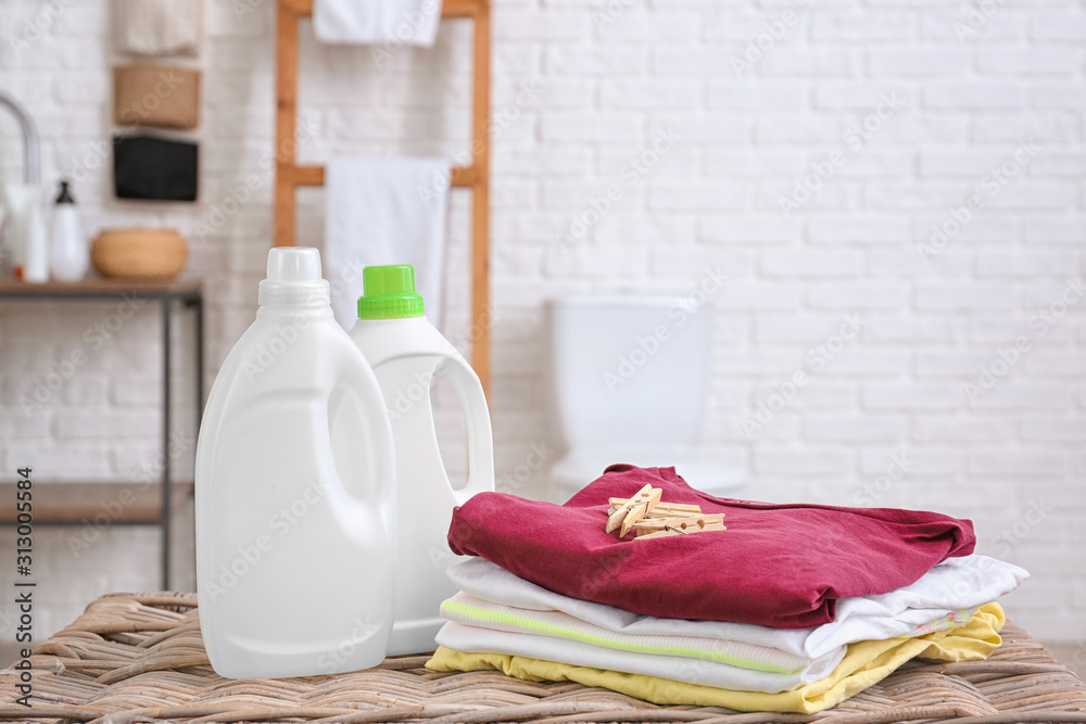 Clean laundry and washing liquid on table in bathroom