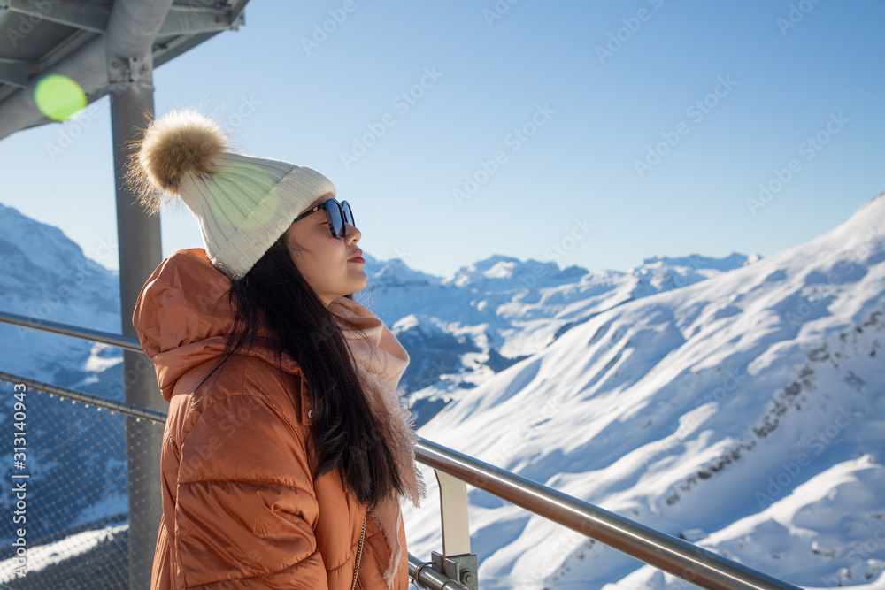 A picture of a beautiful woman looking at a mountain with a lot of snow happily as a holiday vacatio