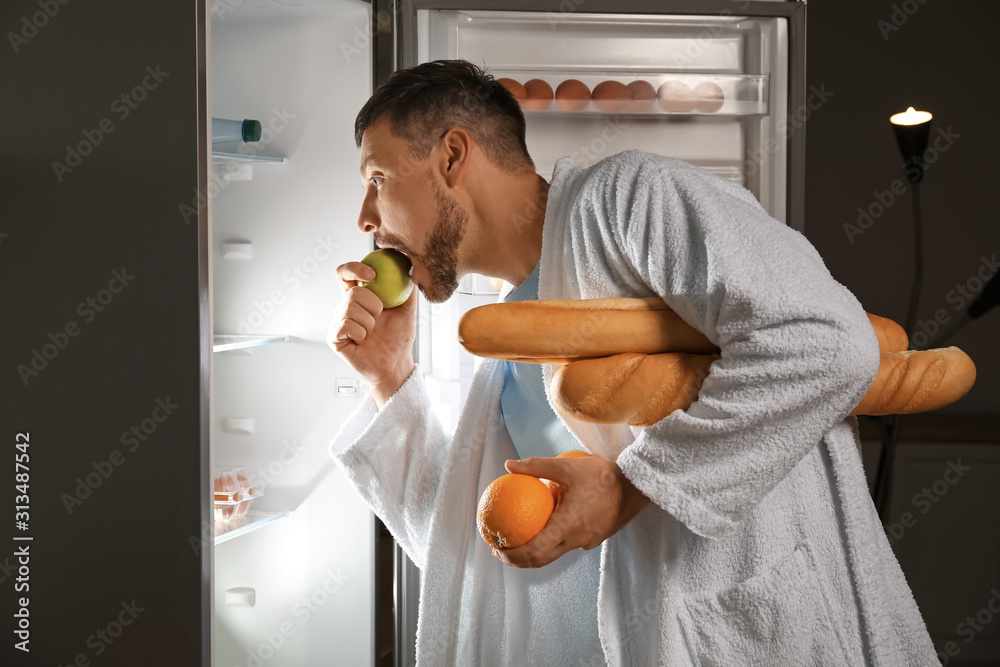 Handsome man choosing food in refrigerator at night