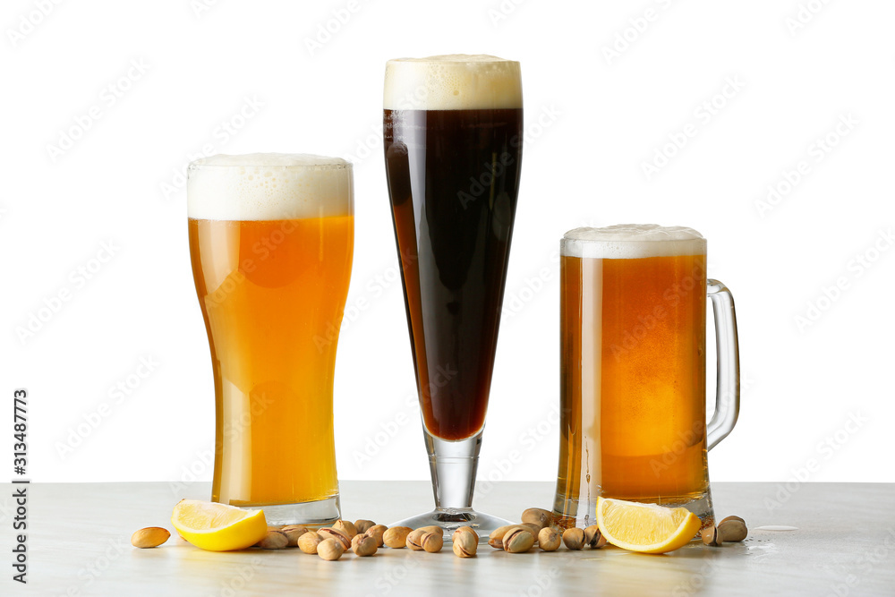 Glasses of different tasty beer with pistachio nuts on white background