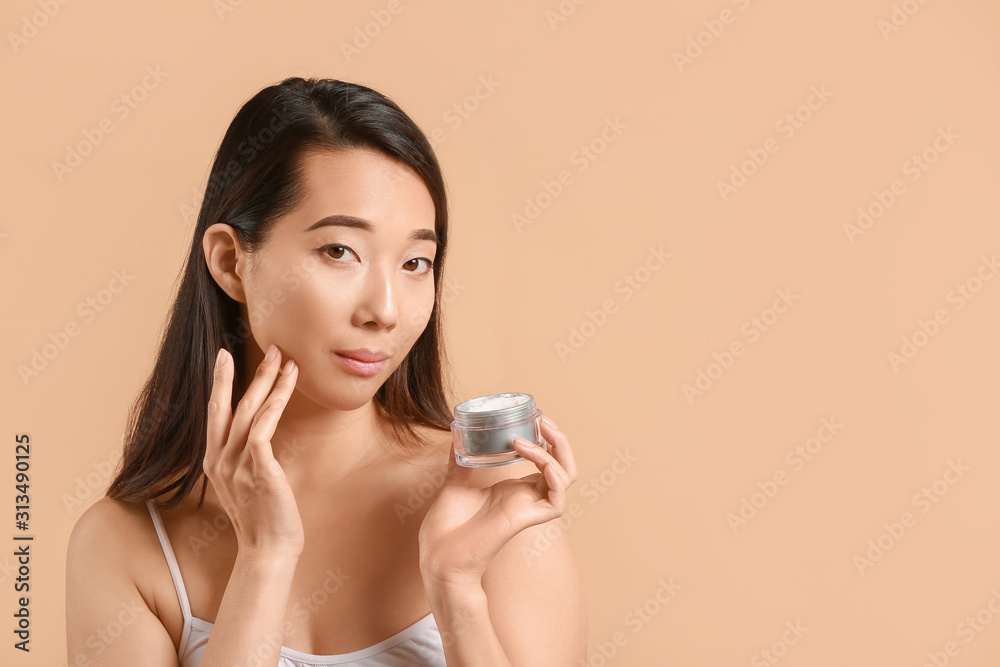 Beautiful young Asian woman with cream on color background