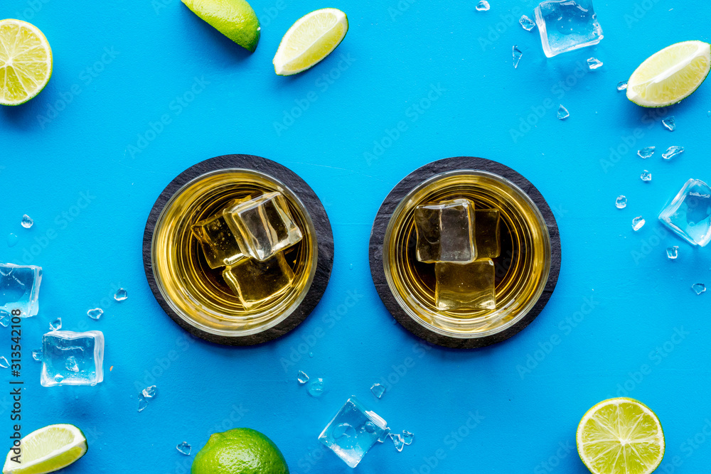 Whiskey near ice cubes on blue background top-down