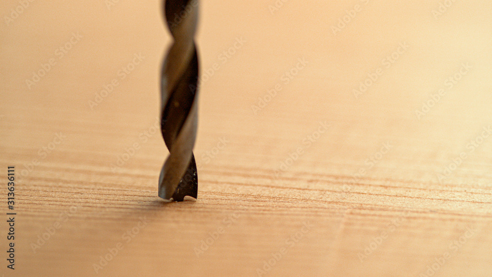 MACRO: Detailed shot of a sharp metal drill resting on a smooth wooden board.