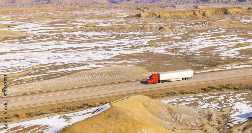 AERIAL: Barren wintry landscape surrounds a cargo truck driving across Utah.