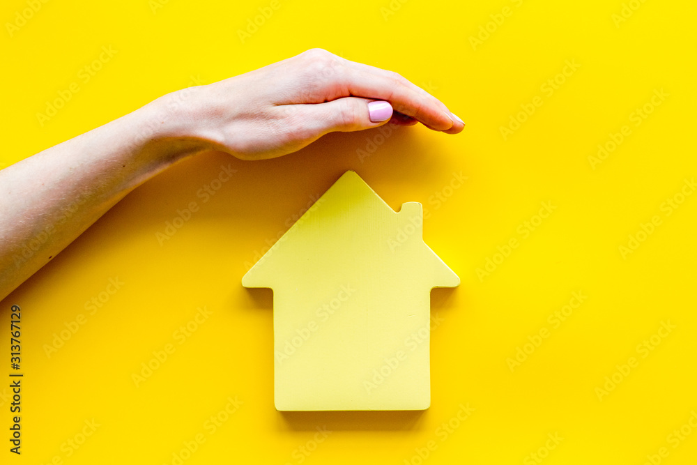 Property insurance concept. Hand defends house cutout on yellow backgound top view copy space