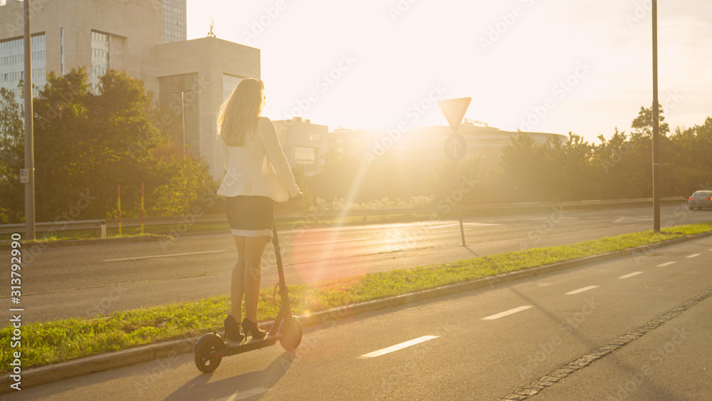 LENS FLARE：一位不知名的女商人在日出时骑着电动踏板车上班。