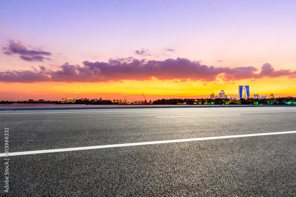 空旷的柏油公路和日落时天空五彩缤纷的苏州城市天际线。