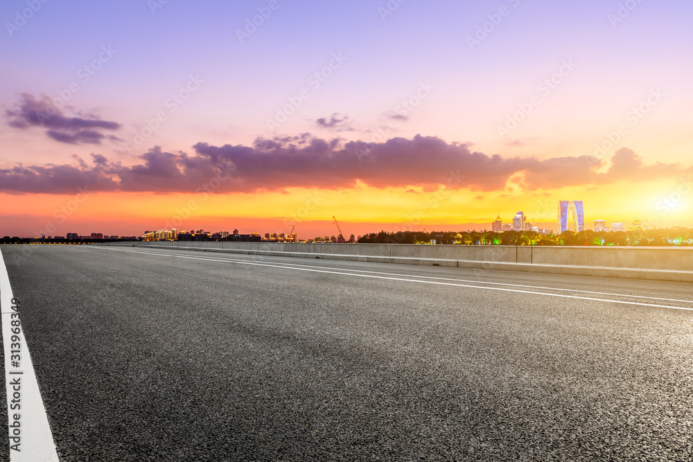 空旷的柏油公路和日落时天空五彩缤纷的苏州城市天际线。