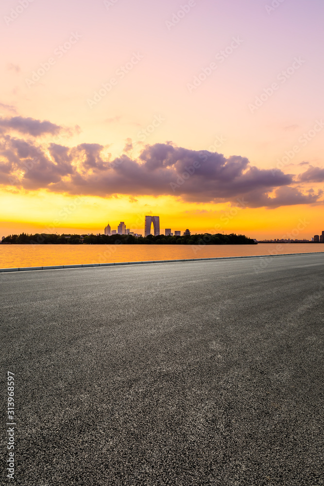 空旷的柏油公路和日落时天空五彩缤纷的苏州城市天际线。