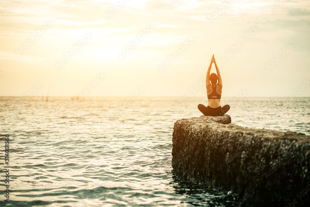 Young Asian woman practicing yoga exercise at quiet rock pier with sea background. Sport and recreat