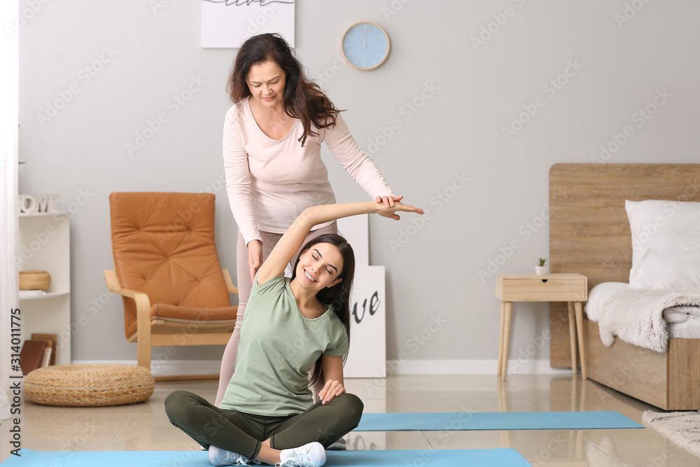 Mature woman helping her adult daughter during yoga practice at home