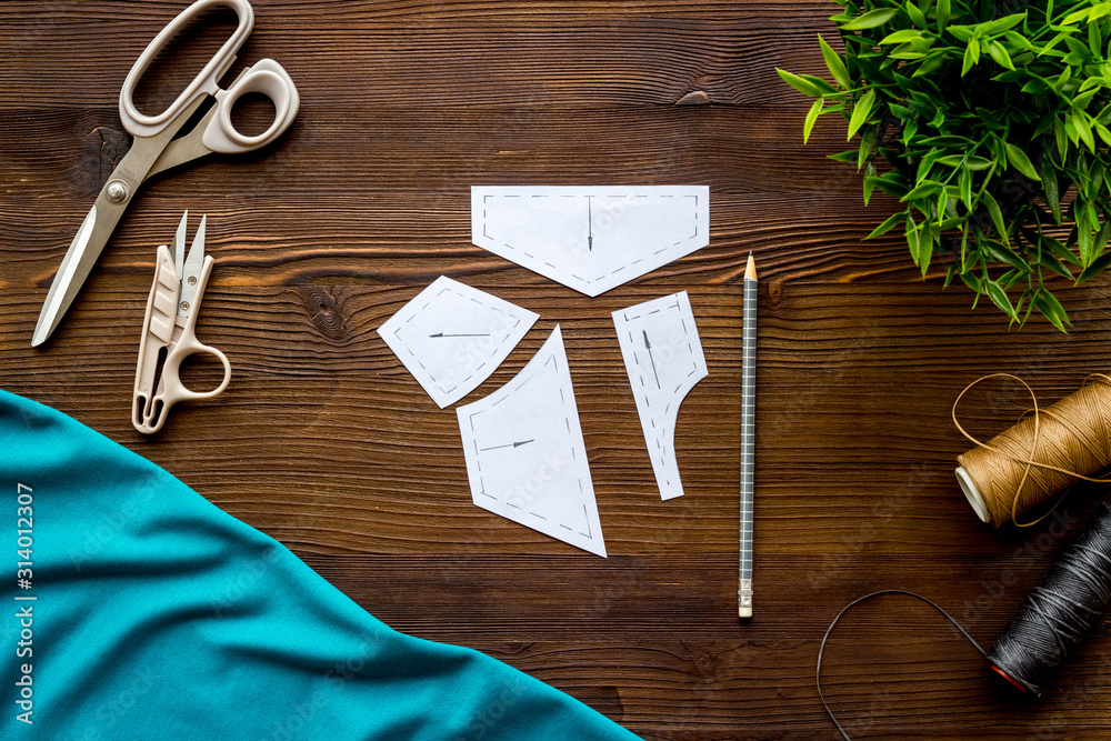 Clothes designer work desk. Pattern, textile, scissors, thread on dark wooden background top-down