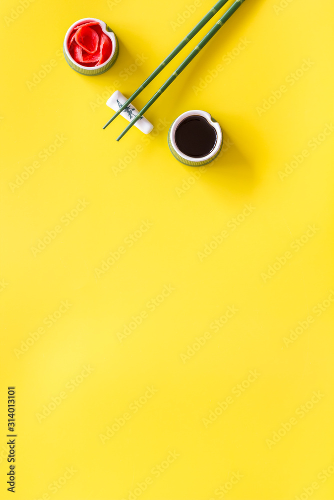 Set of chopsticks for sushi, ginger and soy sause on yellow background top-down frame copy space