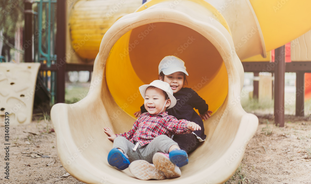 Big sister playing slider tube with her baby brother in the playground.Toddler kid play with sibling