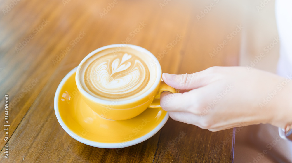 Coffee latte art on woman hand in coffee shop on wooden table in the morning.