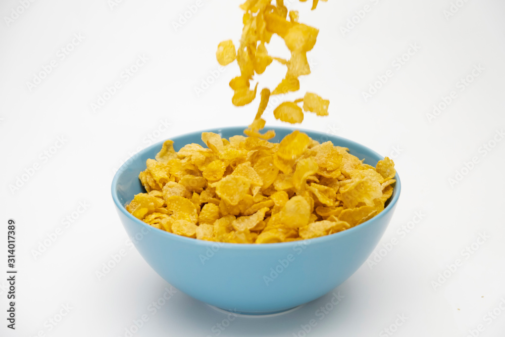 Motion blur of pouring golden cornflakes flowing into the blue bowl isolated on white background