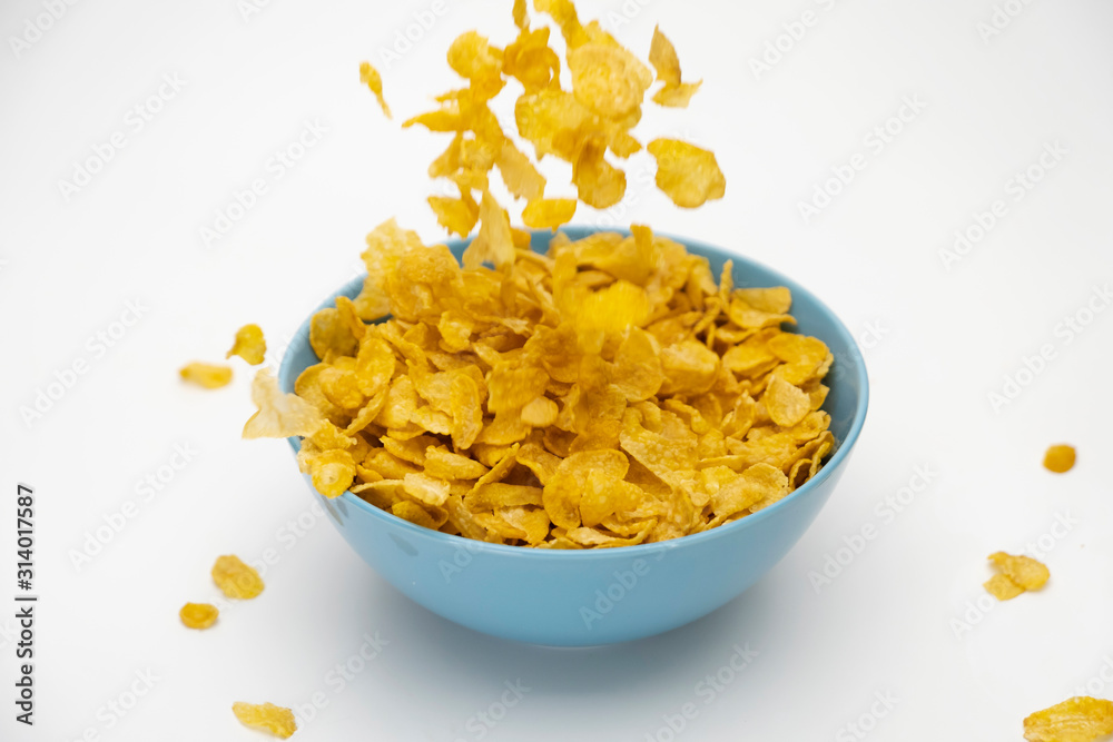 Motion blur of pouring golden cornflakes flowing into the blue bowl isolated on white background