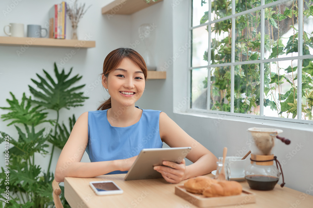 Happy young Asian woman using tablet and drink coffee in morning