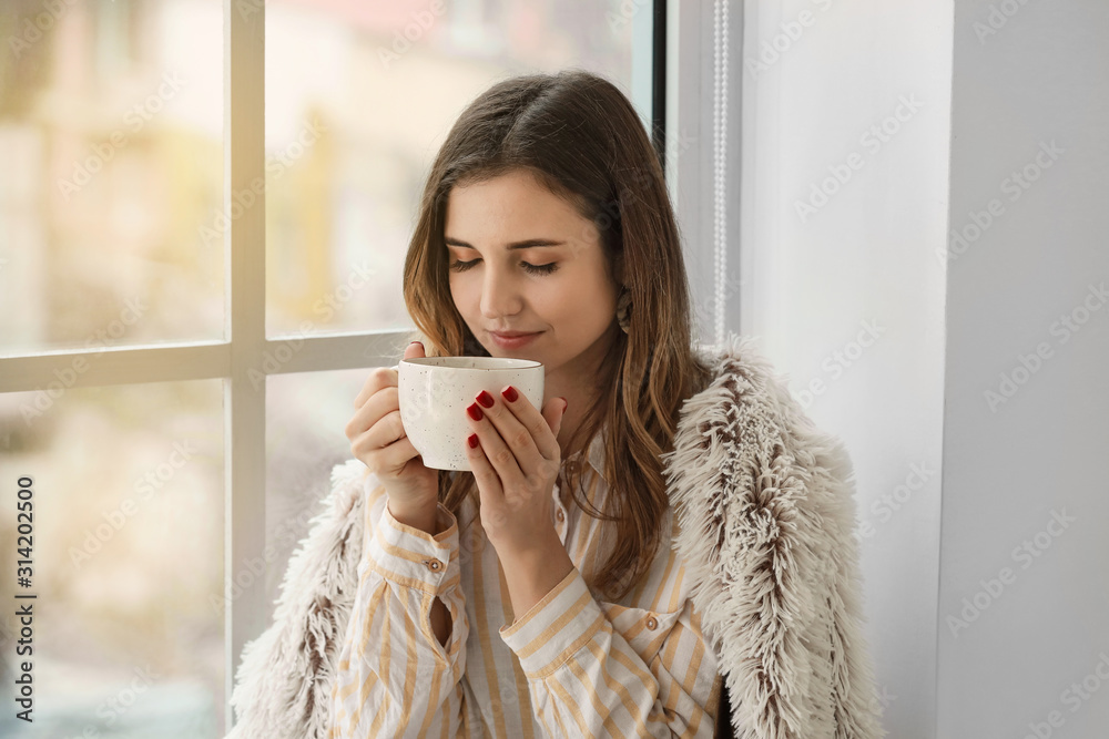 年轻女子在家窗台上喝热茶