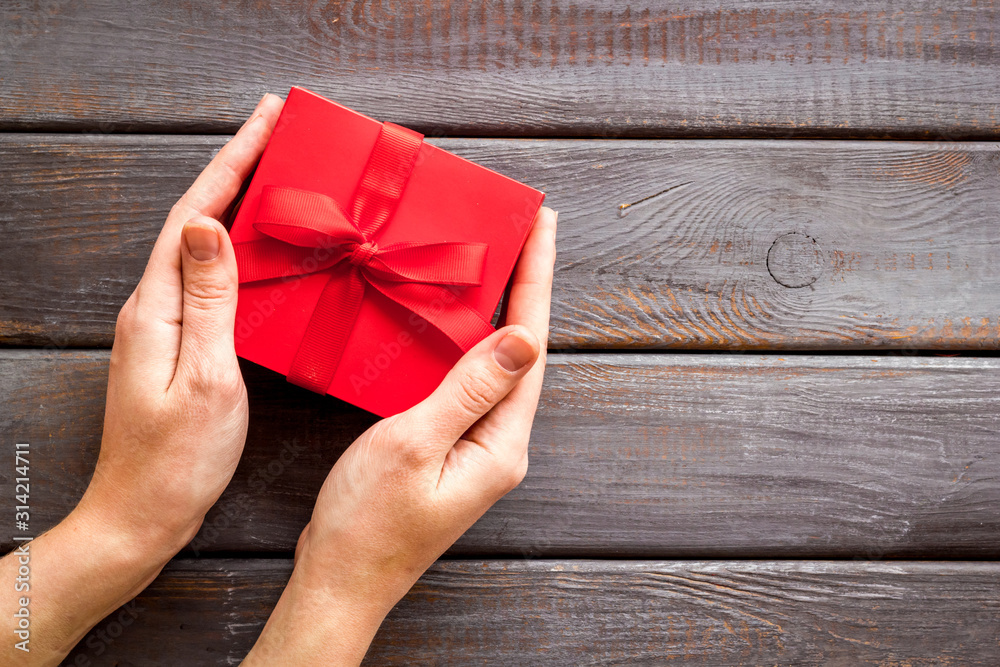 Give a gift on Valentines Day. Women hand hold beautiful red present box on dark wooden background 