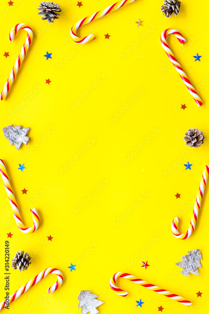 New Year greeting card design. Christmas candy cane, festive tree and balls on yellow desk top-down 