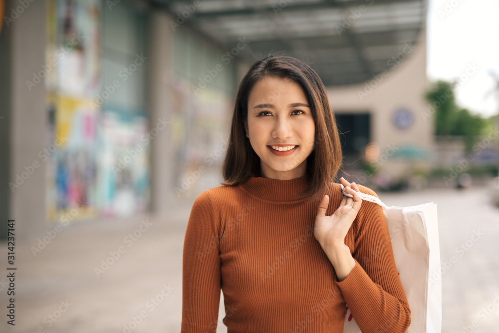 户外购物中心拿着购物袋的快乐亚洲年轻女子的肖像