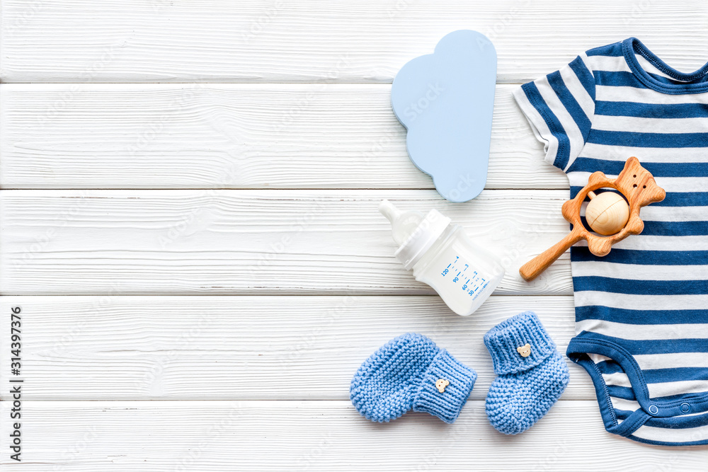 Newborn baby boy set - blue clothes as bodysuit, booties, toys - on white wooden table top-down fram