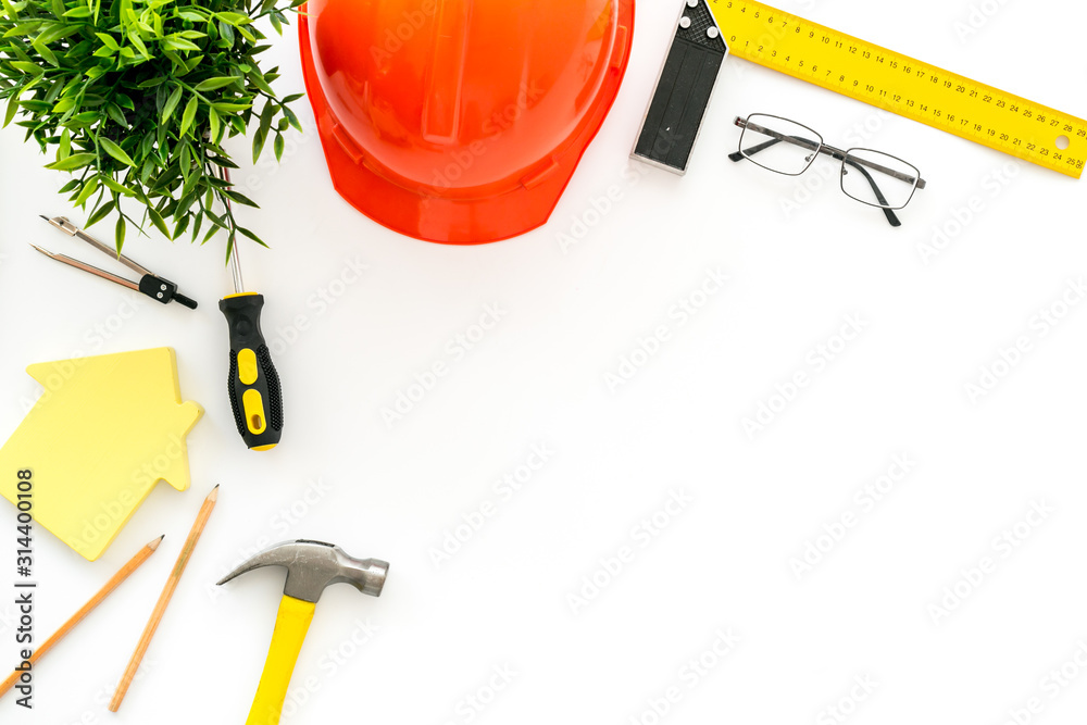 Construction concept. Helmet, tools on work desk, house cutout on white background top-down frame co